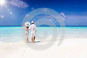 Couple walks hugging down a tropical beach during their vacation