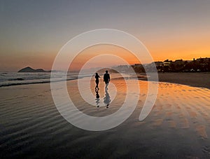 Couple wallking on beach wet sand at sunset