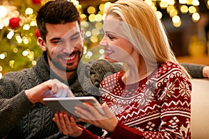 Couple in warm sweaters enjoying with tablet on Christmas