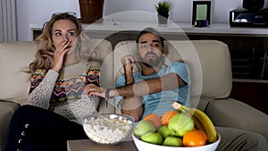 Couple watches a scary movie on the couch in living room