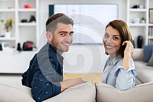 Couple Watches TV together while Sitting on a Couch in the Living Room. Girlfriend and Boyfriend embrace, cuddle, talk