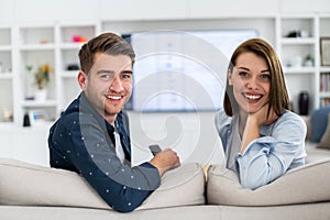 Couple Watches TV together while Sitting on a Couch in the Living Room. Girlfriend and Boyfriend embrace, cuddle, talk