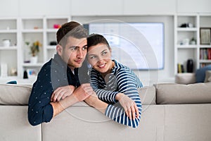 Couple Watches TV together while Sitting on a Couch in the Living Room. Girlfriend and Boyfriend embrace, cuddle, talk