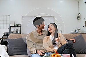 Couple Watches TV together while Sitting on a Couch in the Living Room. Girlfriend and Boyfriend embrace, cuddle, talk