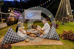 Couple watching a movie at an outdoor cinema film in a tropical garden with christmas lights