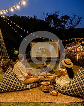 Couple watching a movie at an outdoor cinema film in a tropical garden with christmas lights