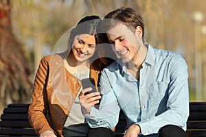 Couple watching a smart phone sitting on a bench