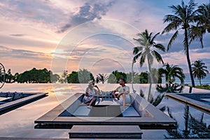 couple watching sunset in infinity pool on a luxury vacation in Thailand, man and woman watching sunset on the edge of a