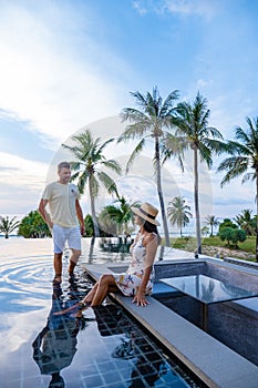 couple watching sunset in infinity pool on a luxury vacation in Thailand, man and woman watching sunset on the edge of a