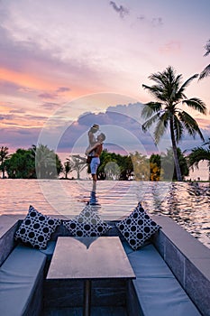 couple watching sunset in infinity pool on a luxury vacation in Thailand, man and woman watching sunset on the edge of a