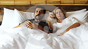 Couple watching television together on bed husband change to favorite channel wife don't want to watch it and snatch remote contro