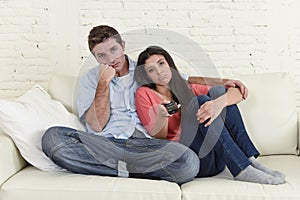 Couple watching television together at home sofa couch looking bored frustrated switching channels