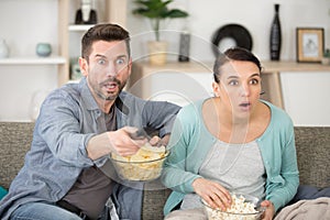 couple watching tv with chips on sofa at home