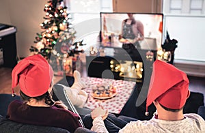 Couple watching tv on Christmas. Happy family holiday at home. Man and woman on couch relaxing with tree, decorations, lights.