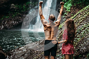 Couple at the waterfall, rear view. Honeymoon trip. Couple on vacation in Bali. A couple in love travels the world.