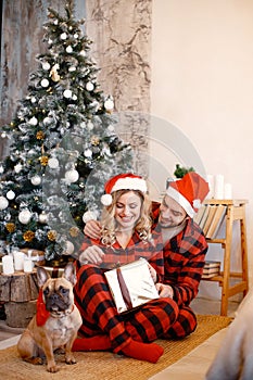 Couple wearing christmas plaid red pajamas sitting on the floor with a dog