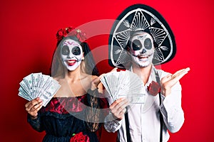 Couple wearing day of the dead costume holding dollars celebrating victory with happy smile and winner expression with raised