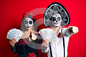 Couple wearing day of the dead costume holding dollars pointing with finger to the camera and to you, confident gesture looking