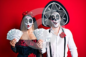 Couple wearing day of the dead costume holding dollars scared and amazed with open mouth for surprise, disbelief face