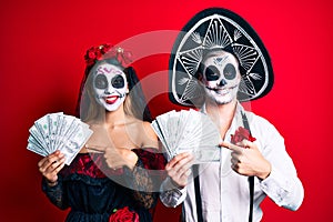 Couple wearing day of the dead costume holding dollars smiling happy pointing with hand and finger