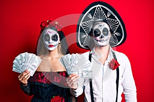 Couple wearing day of the dead costume holding dollars thinking attitude and sober expression looking self confident