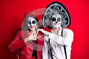 Couple wearing day of the dead costume over red smiling in love showing heart symbol and shape with hands