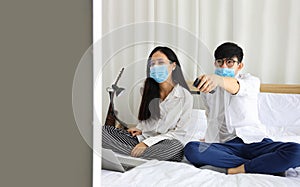 Couple wearing facial mask watching news on television while working at home during quarantine from coronavius or covid-19