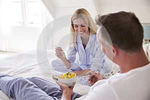 Couple Wearing Pajamas Sitting In Bed Eating Breakfast Together