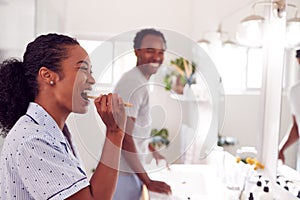 Couple Wearing Pyjamas Standing In Bathroom At Sink Brushing Teeth In The Morning