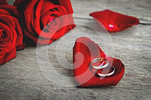 Couple wedding rings on red rose petal with red rose flower bouquet on wooden background