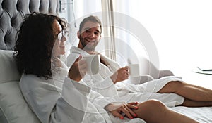 Couple in white bathrobe on a bed in a hotel.