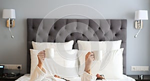 Couple in white bathrobe with cups of coffee on a bed in a hotel. Morning in the hotel room