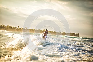 Couple in white on sea beach in waves at sunset