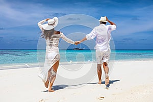 Couple in white summer clothes running happy on a tropical beach