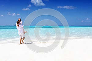 Couple in white summer clothing hugging on a tropical beach