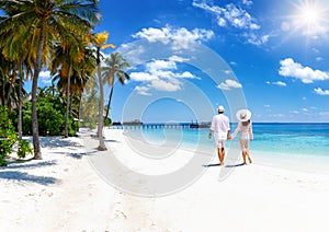 A couple in white summer clothing walks down a paradise beach