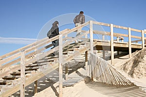 Couple in winter wooden path stairs boards through the dunes to the beach of lacanau sea france