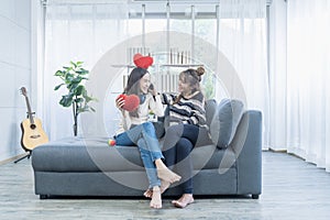 Couple woman in love smiling and holding red hearts on sofa in the living room. Lifestyle of couple loving woman happy in romance