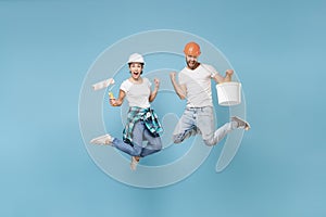 Couple woman man in protective helmet hardhat jump with paint bucket, roller isolated on blue background. Instruments