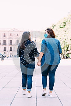 Couple of women with a face mask walking hand in hand