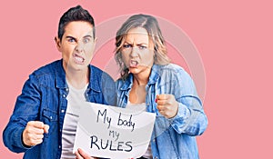 Couple of women holding my body my rules banner annoyed and frustrated shouting with anger, yelling crazy with anger and hand