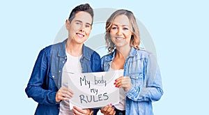 Couple of women holding my body my rules banner looking positive and happy standing and smiling with a confident smile showing