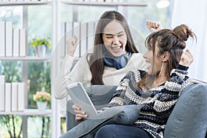 Couple women rejoicing. Two Young Woman Talking and rejoicing. Two women use tablets on the sofa in the living room