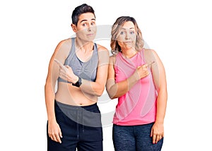 Couple of women wearing sportswear pointing to both sides with fingers, different direction disagree