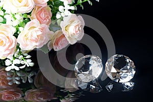 Couple of wonderful pure diamonds and bouquet of tea roses with reflection on black mirror background close up view. Jewelry