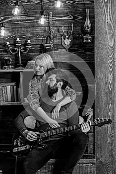 Couple in wooden vintage interior enjoy guitar music. Lady and man with beard on dreamy faces hugs and plays guitar