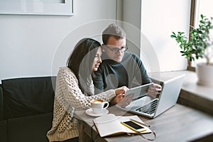 Couple working in cafe with tablet, laptop, smartphone, notepad