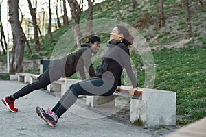 Couple working out in park outdoors. Active athletic african couple doing push-ups on a bench in the park. Exercising