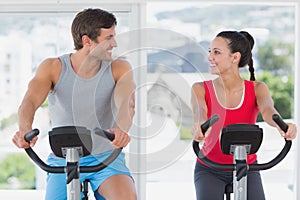 Couple working out at spinning class in bright gym