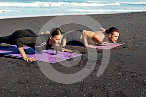 Couple Workout On Beach. Handsome Man And Sexy Woman In Fashion Sporty Outfit Doing Push-Ups On Yoga Mat In Morning.